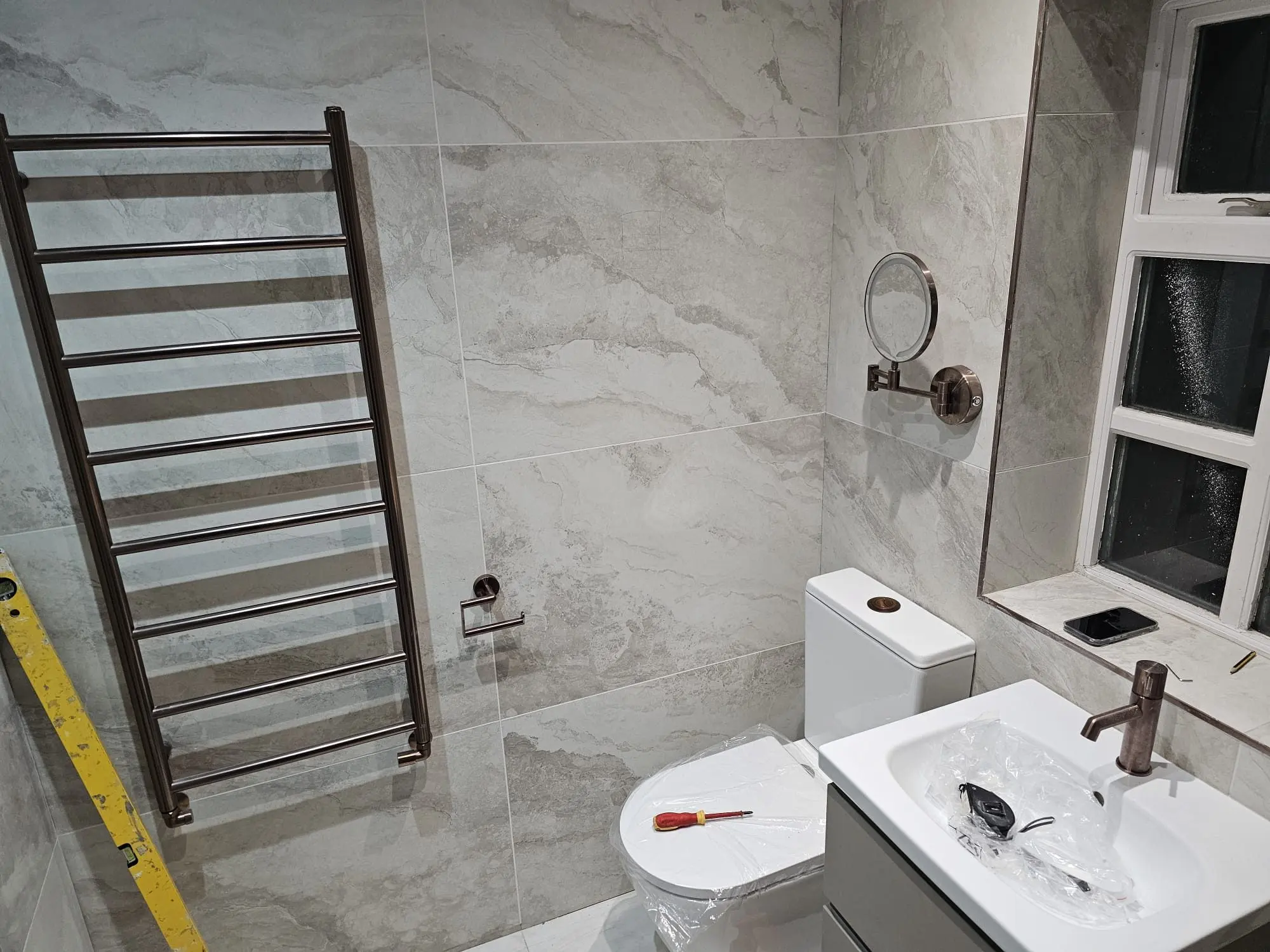 Brushed bronze towel ladder and WC against large-format marble-look tiles