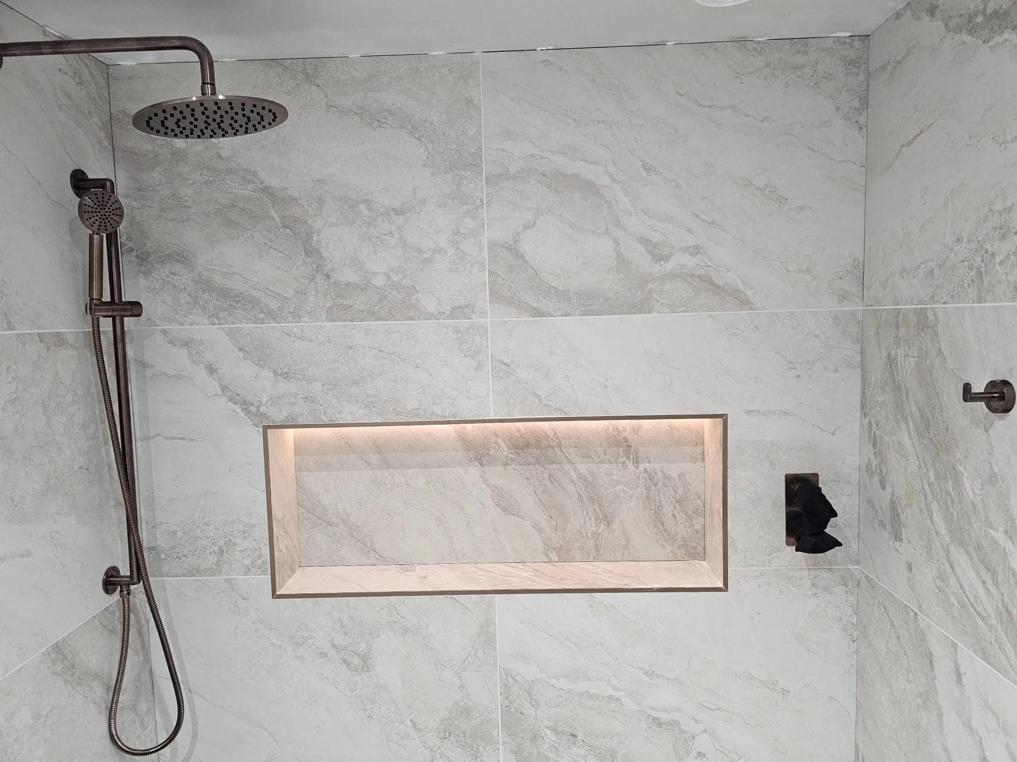 Walk-in shower with brushed bronze rainfall head and lit storage niche