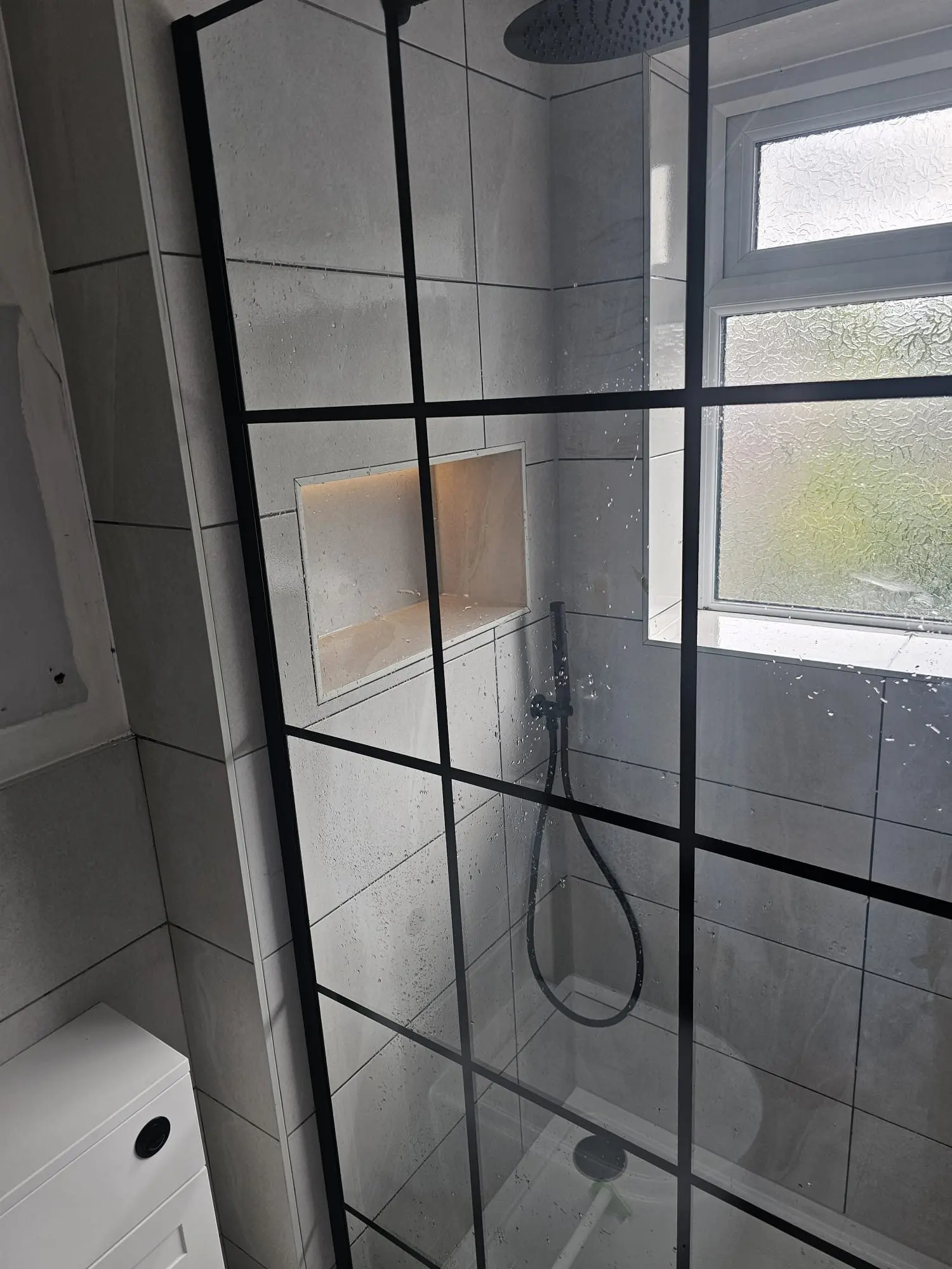Walk-in shower with black grid screen, hand shower and illuminated storage niche