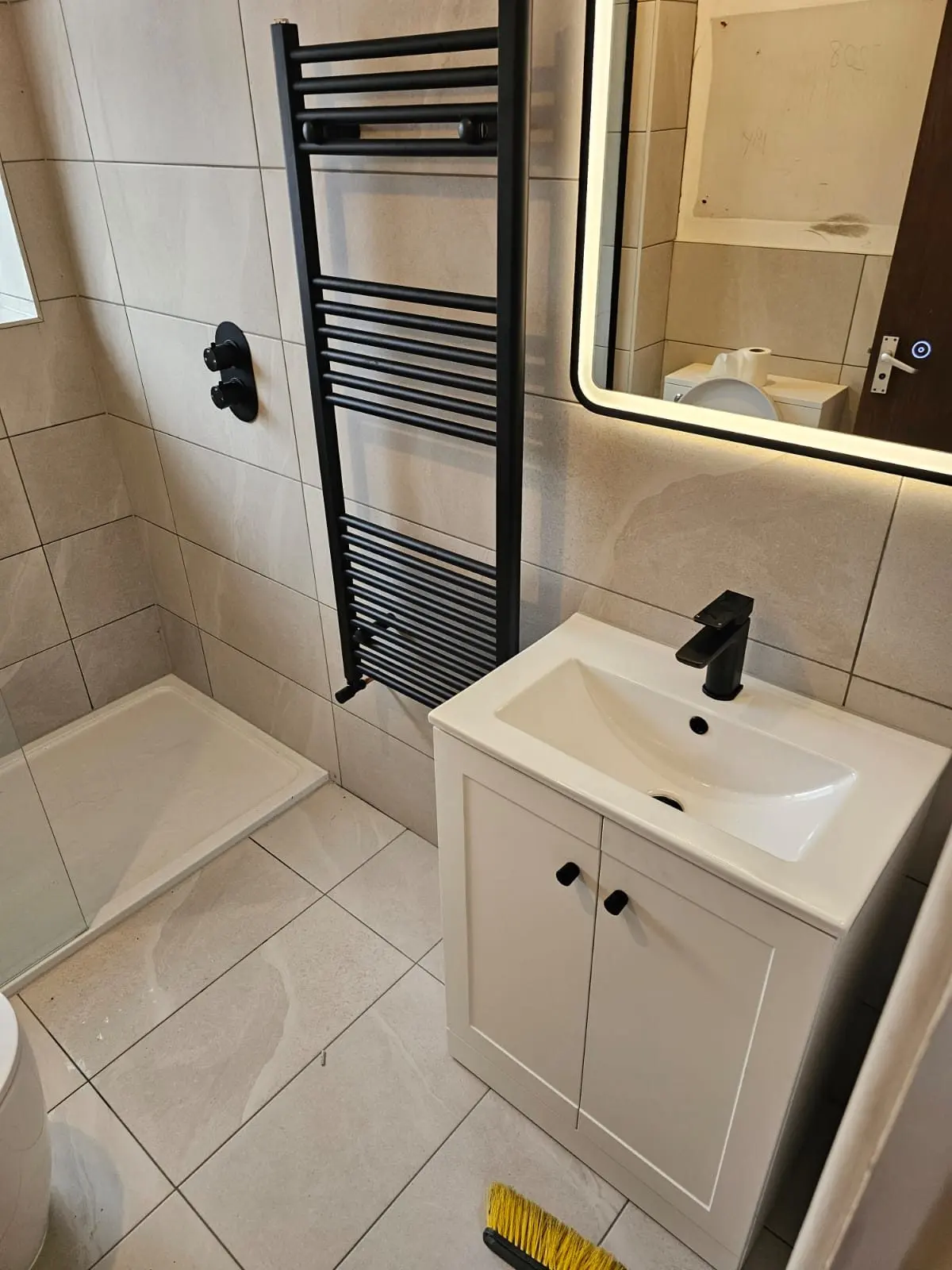 Cloakroom with black ladder radiator, white vanity and backlit mirror