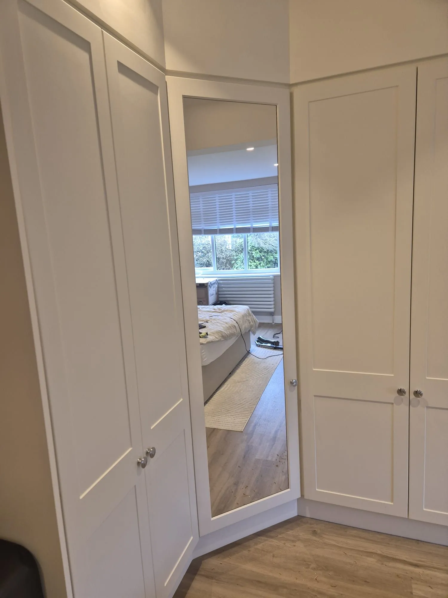 Full-height mirrored corner door between shaker wardrobe runs