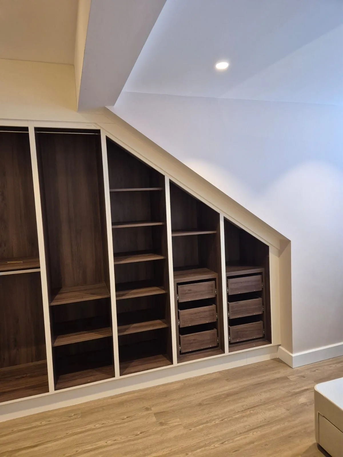 Walnut wardrobe interior with shelving, hanging rail and drawers built under a sloping roof