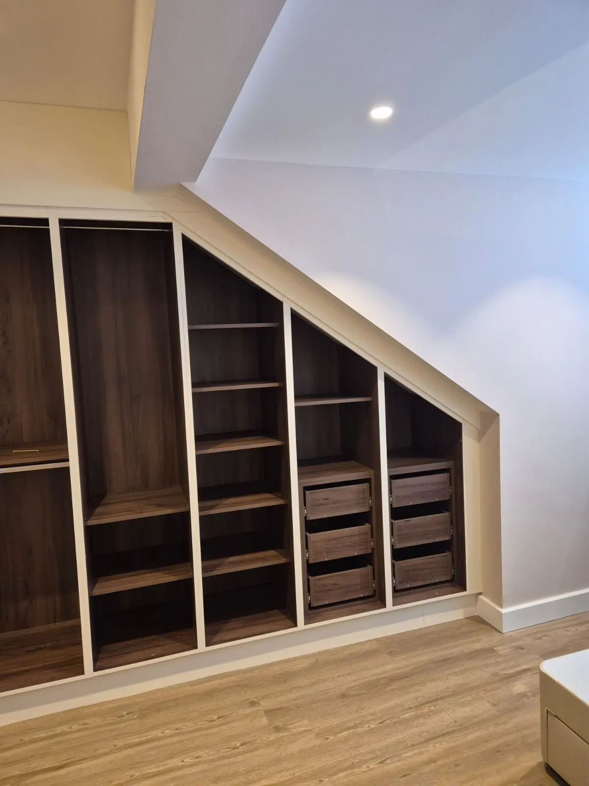 Walnut wardrobe interior with shelving, hanging and drawers built under a sloping roof