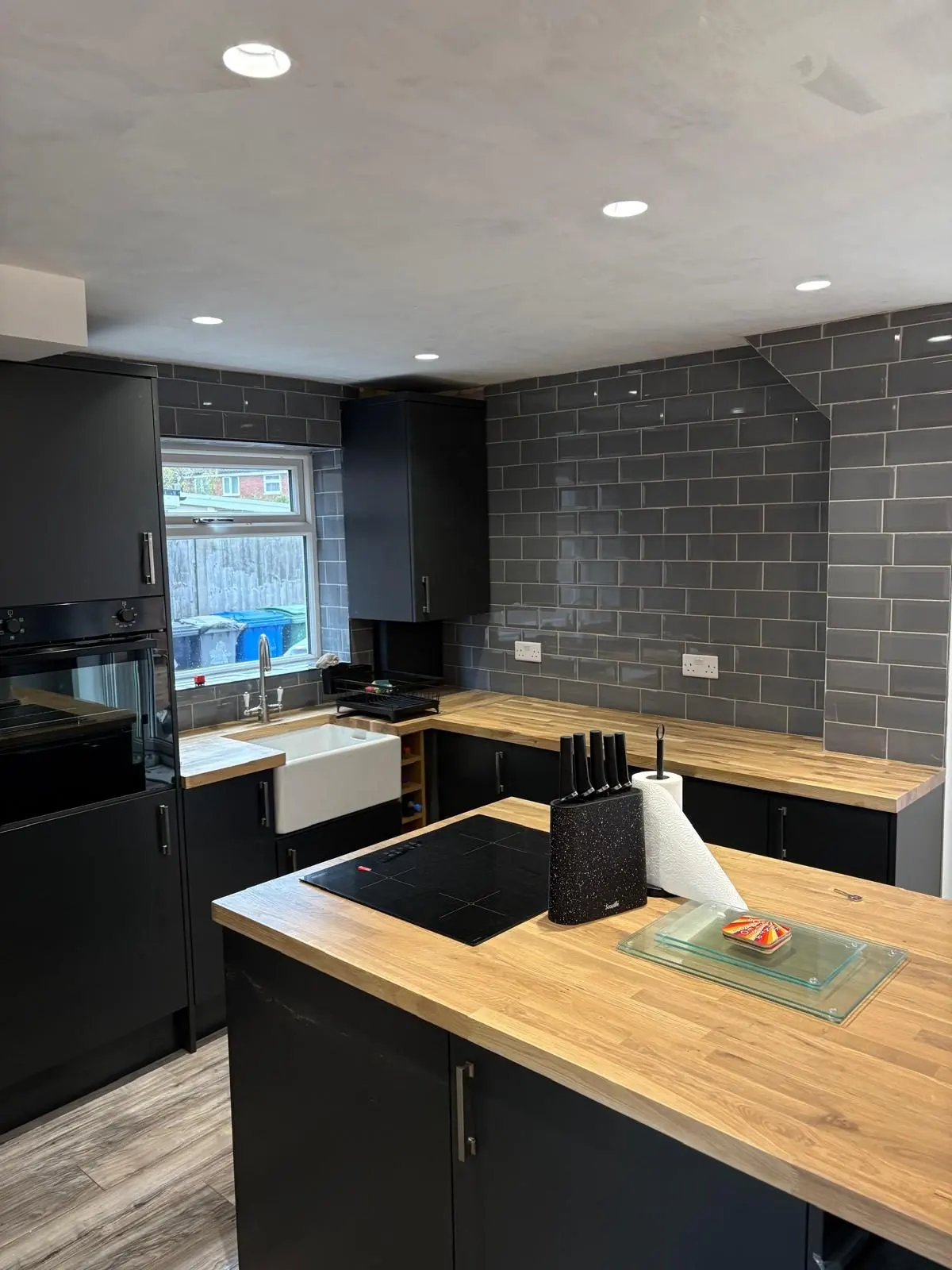 Matt black kitchen with oak island, Belfast sink and grey metro tiled chimney breast, fitted by CKC
