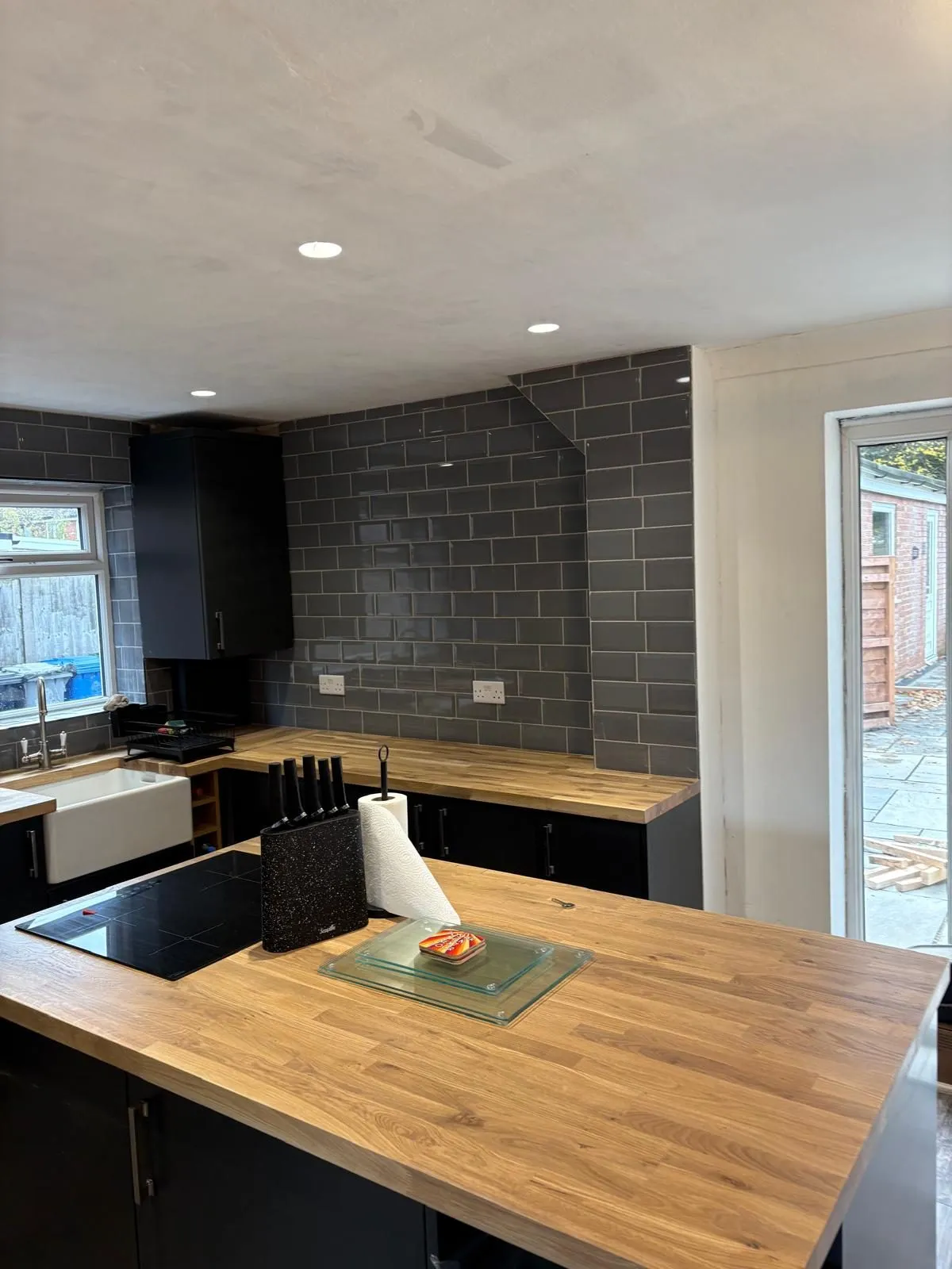 A finished CKC kitchen — matt black units, solid oak worktops and grey metro tiles