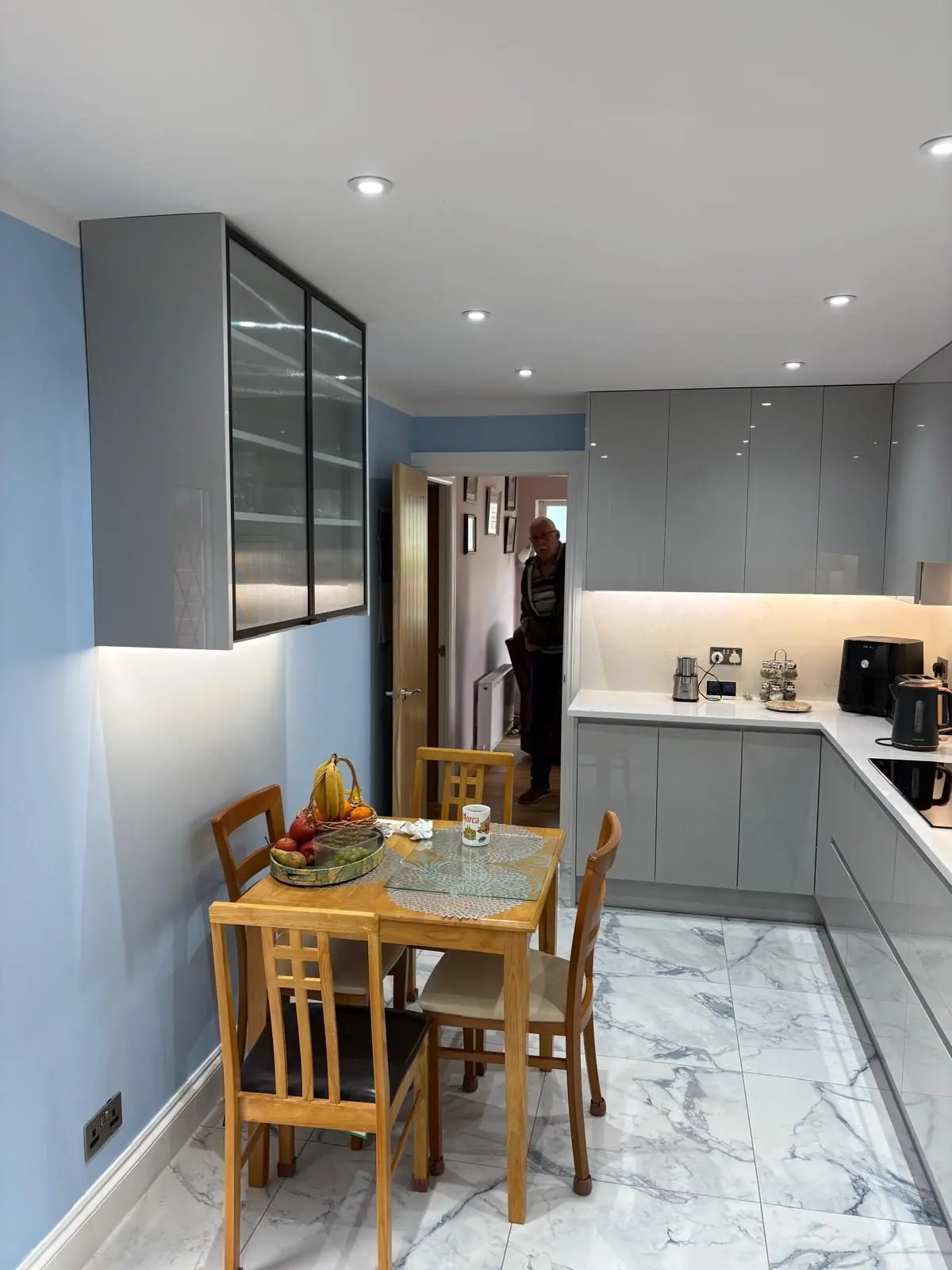Grey gloss kitchen with glazed wall cabinet and dining table on marble-look porcelain