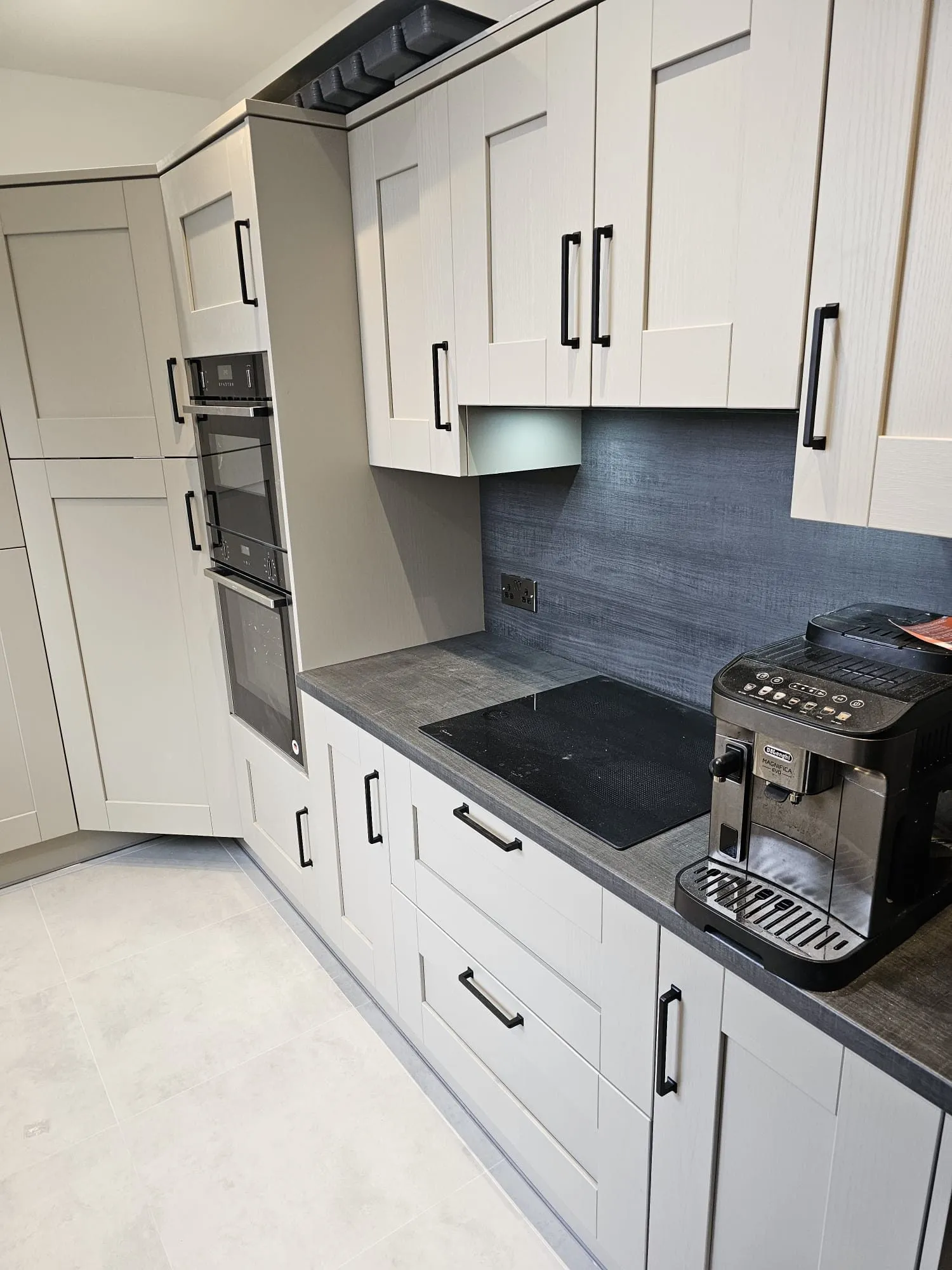 Grey shaker kitchen hob run with black handles, dark worktop and under-cabinet lighting