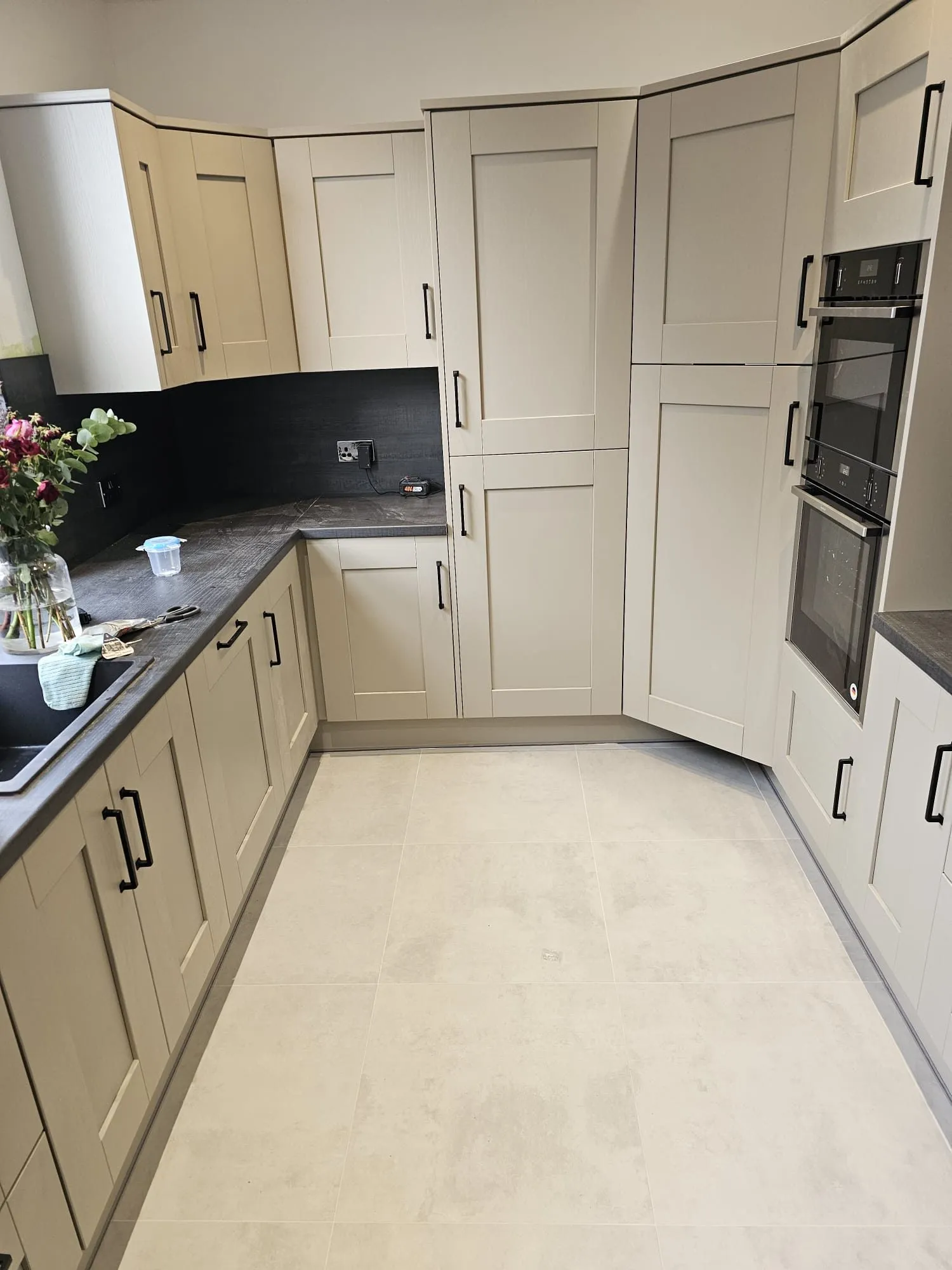 Light grey shaker kitchen with matt black handles, dark worktop and dark slate splashback, integrated double oven